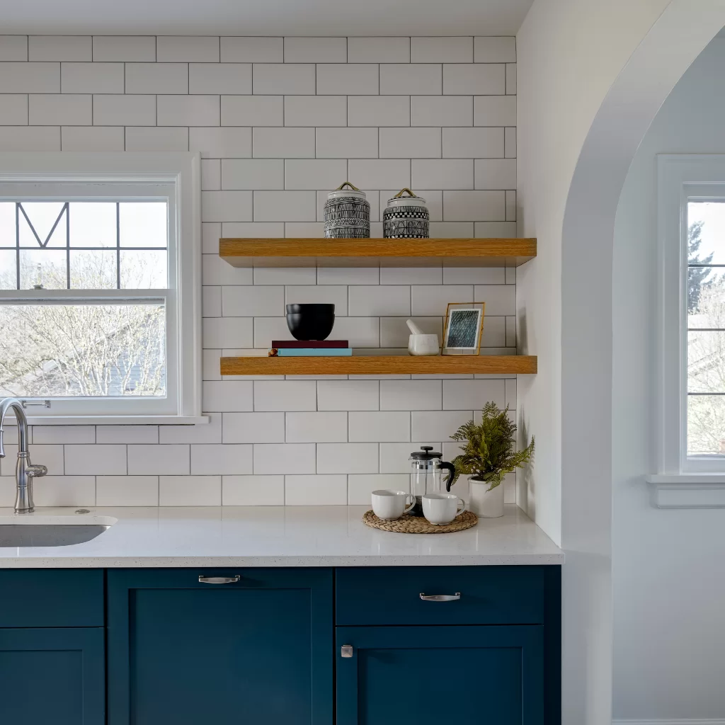 Compact kitchen with white backsplash, wooden shelves, and navy base cabinets
