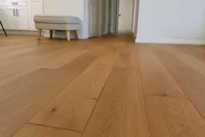Room with damaged hardwood flooring showing visible seam cracks caused by uneven subfloor