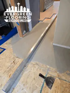 Self-leveling compound applied over plywood subfloor with straightedge for flatness check during flooring prep